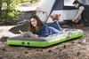 A young woman is reading a book on an inflatable mattress outdoors, with a tent and another person in the background. Podgląd zdjęcia produktu