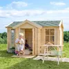 Two children playing in and around a wooden playhouse in a grassy outdoor setting. Produktbild-Vorschau