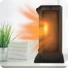 A black electric heater is shown on a white surface, emitting orange heat waves. Beside it are stacked white towels and a potted green plant. Voir les images du produit
