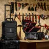 A collection of tools and toolboxes are displayed on a wooden wall and a workbench. Produktbild-Vorschau