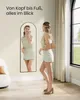 A woman is standing in front of a full-length mirror, checking her outfit. The mirror is tall and arched, reflecting her from head to toe. The room appears to be a bedroom or dressing area, with soft lighting and neutral decor. Produktbild-Vorschau
