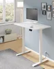 A white height-adjustable desk with a computer and keyboard is shown in a room with a window and a cabinet. Podgląd zdjęcia produktu
