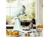 A light green SMEG stand mixer is shown in a kitchen setting, with muffins and baking ingredients around it. Náhled obrázku produktu