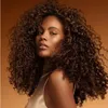 A woman with curly hair is shown from the chest up, looking towards the camera. Produktbild-Vorschau