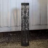 A black, solar-powered pathway light with a decorative, tree-like pattern is shown standing on gravel in front of a white, corrugated wall. Produktbild-Vorschau