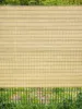 A beige shade screen is attached to a green metal fence, with green grass visible below. Produktbild-Vorschau