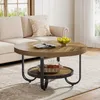 A round coffee table with a lower shelf is placed in a living room setting, next to a sofa. Náhľad obrázku produktu