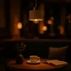 A dimly lit room with a pendant lamp, a cup of coffee, a book, and a vase with greenery on a table. Náhled obrázku produktu
