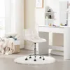 A cream white office stool is placed on a fluffy white rug in front of a white dressing table with various cosmetic products on it. A woven basket filled with blankets and pillows is to the left of the stool, and a window with sheer curtains is in the back Produktbild-Vorschau