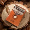 A kalimba instrument is placed on a wooden surface with some dried leaves. Produktbild-Vorschau