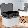 A kitchen compost bin with its lid open, showing the removable inner container. The background shows a blurred kitchen counter with fruit and flowers. Produktbild-Vorschau