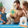 A family (father, mother, daughter) is on a couch, and the father is opening a gift for the daughter. A handprint keepsake is in the foreground. Produktbild-Vorschau