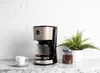A coffee maker with a cup of coffee and a plant on a marble countertop. Náhled obrázku produktu