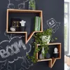 Two wooden shelves shaped like speech bubbles are mounted on a dark wall with chalk drawings. One shelf holds books and decorative items, while the other has plants and vases. Produktbild-Vorschau