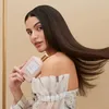 A woman is holding a bottle of hair product, with her hair flowing. Náhled obrázku produktu
