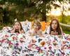 Three young girls are lying on a bed outdoors, with a colorful duvet cover featuring birds and flowers. Produktbild-Vorschau