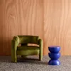 A green armchair and a blue side table are placed on a speckled floor in front of a wooden wall. Anteprima dell’immagine prodotto