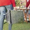 A person is carrying a portable barbecue grill in a backyard setting. Produktbild-Vorschau