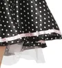 A close-up view of the hem of a black polka dot dress with a pink ribbon trim and a white tulle underskirt. Produktbild-Vorschau