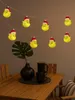 A string of Grinch-themed LED lights hangs above a wooden table set with a vase, a plant, and coffee cups. Produktbild-Vorschau