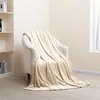 A plush blanket draped over an armchair in a room with a bookshelf and a window. Produktbild-Vorschau