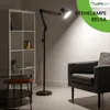 A modern living room scene featuring a black floor lamp, a bookshelf, and an armchair. Produktbild-Vorschau