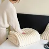 A person is folding a soft, beige blanket on a bed. Produktbild-Vorschau