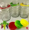 Three glass jars with colored handles and lids, along with grapes and a raspberry, are displayed on a white surface. Produktbild-Vorschau