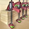 Several red and black clamps with green accents are holding together a stack of plywood. Náhled obrázku produktu