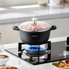 A black pot with a glass lid filled with food is placed on a gas stove with a blue flame. Produktbild-Vorschau