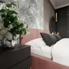 A bedroom scene with a pink upholstered bed, pillows, and a nightstand with flowers. Produktbild-Vorschau