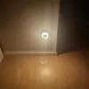 A small LED night light is mounted on a wall above a wooden floor. Produktbild-Vorschau