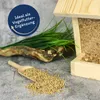 A wooden bird feeder filled with birdseed, with a scoop of birdseed in the foreground and artificial grass and a branch in the background. Produktbild-Vorschau