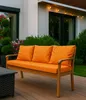 An outdoor sofa with orange cushions sits on a wooden deck, with a house and garden in the background. Anteprima dell’immagine prodotto