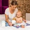 A mother and baby are sitting on a bed, with the mother holding a toy for the baby. Produktbild-Vorschau