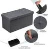 A dark gray storage ottoman is shown with various close-up views highlighting its features, including a hand pressing on the padded seat, a close-up of the tufted lid, a hand pulling on the fabric handles, and a separate black storage container. Anteprima dell’immagine prodotto