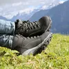 A person wearing hiking boots is resting on a grassy hill with mountains in the background. Produktbild-Vorschau