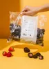 A bag of chocolate-covered strawberries is held by a hand, with loose strawberries and chocolate-covered strawberries on a yellow platform. Produktbild-Vorschau