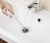 A hand is using a cleaning brush to clean a sink drain while water is running from the faucet. Produktbild-Vorschau