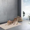 A kitten stretching on a beige mat in a modern bathroom with a large window overlooking a lake. Produktbild-Vorschau