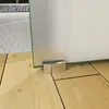 Close-up of the bottom of a glass sliding door on a wooden floor, with a small metal support at the base. Produktbild-Vorschau
