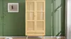 A wooden wardrobe with rattan doors stands against a green wall, with a framed picture and a floor lamp in the scene. Produktbild-Vorschau