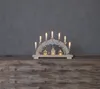 A wooden Christmas arch with lights and small houses, placed on a wooden surface against a gray background. Podgląd zdjęcia produktu