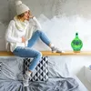 A woman is sitting on a shelf above a bed, with an aroma diffuser on the shelf next to her. Voir les images du produit