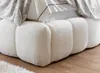A close-up view of the textured white base of a bed, with a fluffy blanket and pillows visible at the top. Náhled obrázku produktu