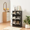 A shoe cabinet with multiple shelves and flip-down doors, filled with various shoes, is shown in a room with a mirror and a plant. Produktbild-Vorschau