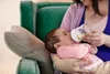 A mother is feeding her baby with a bottle while sitting on a couch. Produktbild-Vorschau