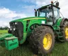 A green tractor is parked in a grassy field under a blue sky with white clouds. Produktbild-Vorschau
