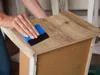 A person is applying wood-look contact paper to the edge of a piece of furniture. Produktbild-Vorschau