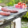 Burgers cooking on a portable barbecue grill with a bowl of cherry tomatoes in the background. Produktbild-Vorschau